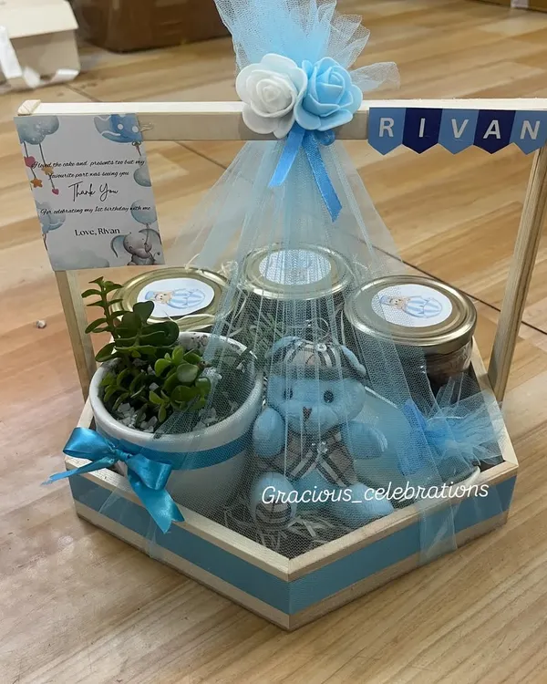 This is one of my absolute favorite designs for a baby boy's first birthday. The hexagonal wooden tray is filled with goodies like a live succulent plant, jars of treats, and a cute teddy bear. We personalize it with the baby's name and a thank you card to make it extra special for your guests.