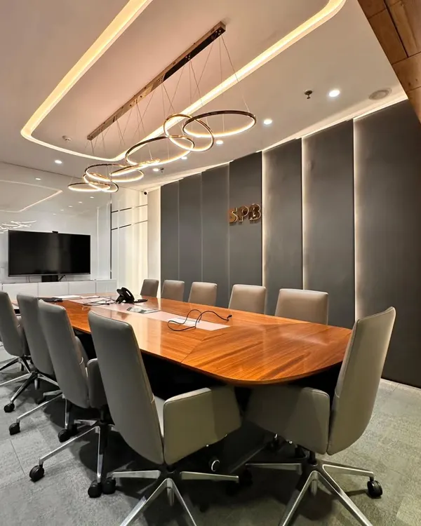 This is a full view of a boardroom designed for focus and impact. The long, polished wooden table is complemented by ergonomic chairs, while the fabric-paneled wall provides sound absorption for confidential discussions.
