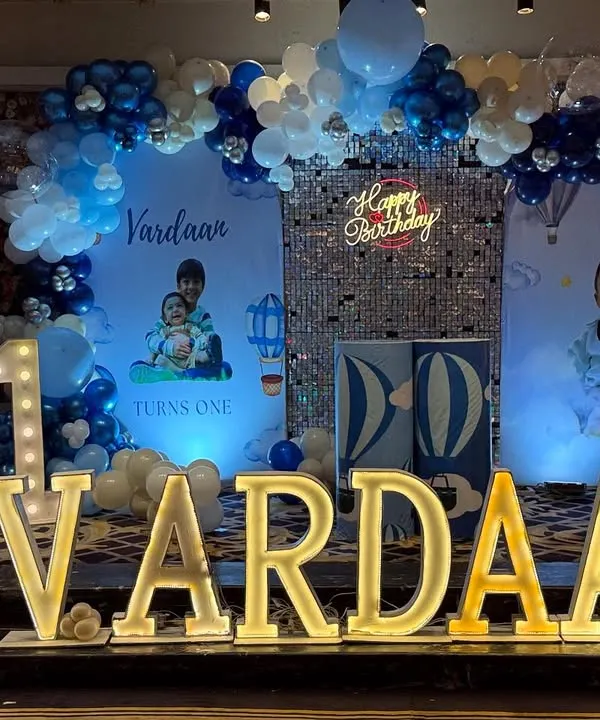 A classic blue and white hot air balloon and teddy bear theme for Vardaan's first birthday. The stage features custom backdrops, a silver sequin panel, and a beautiful balloon arch.