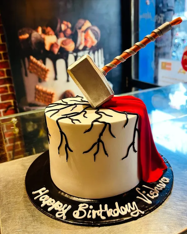 A cake worthy of a hero. This Thor-themed cake features an edible Mjolnir hammer smashing into the top, with lightning cracks and a flowing red cape made of fondant.