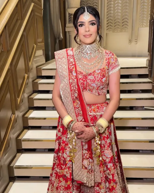 A full-length view of a radiant bride in her stunning red floral lehenga. The makeup is balanced to complement the intricate outfit, ensuring she looks breathtaking from every angle.
