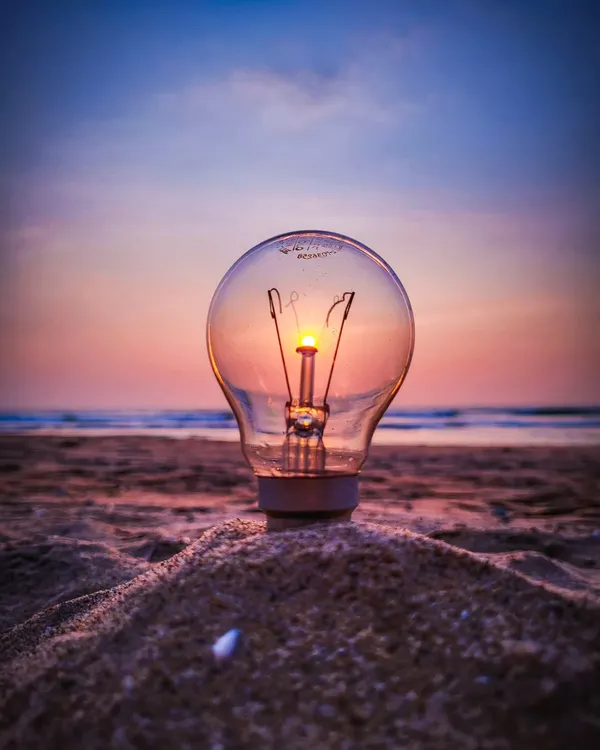 A creative sunset shot where the sun perfectly aligns with the filament of a lightbulb placed in the sand. It’s a fun illusion that makes it look like the sun is powering the bulb.