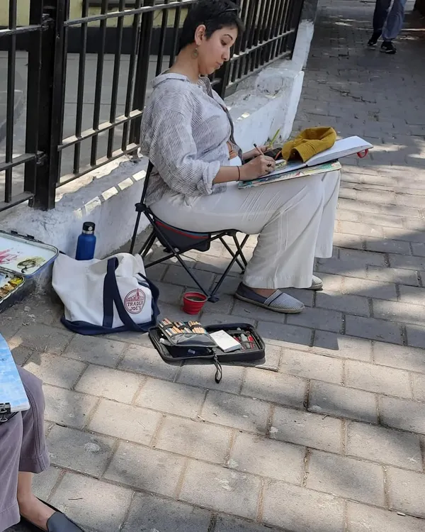 Here I am, set up on a sidewalk with my portable chair and sketchbook. This is my element, urban sketching with my local artist group, capturing the daily life of the city.