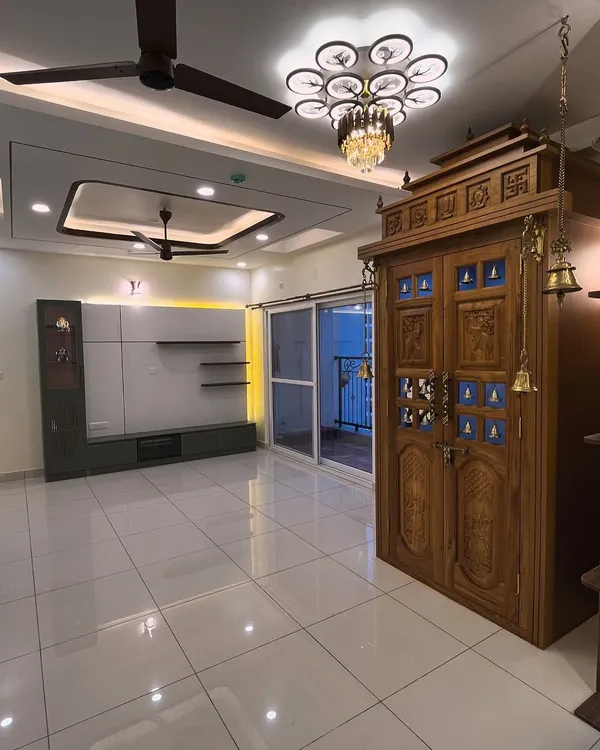 A picture-perfect view of a traditional teak wood pooja unit with carved doors and brass bells, standing next to a contemporary TV unit. This shows how we can blend different styles in one space.