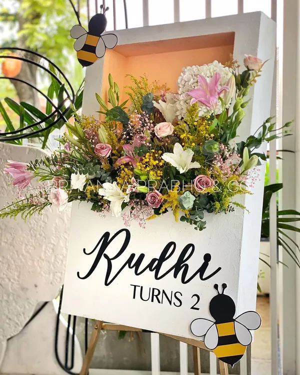 A custom welcome sign for a second birthday party with a 'Garden Party' theme. We created a beautiful shadow box filled with fresh flowers and added cute bee cutouts to match the whimsical theme.