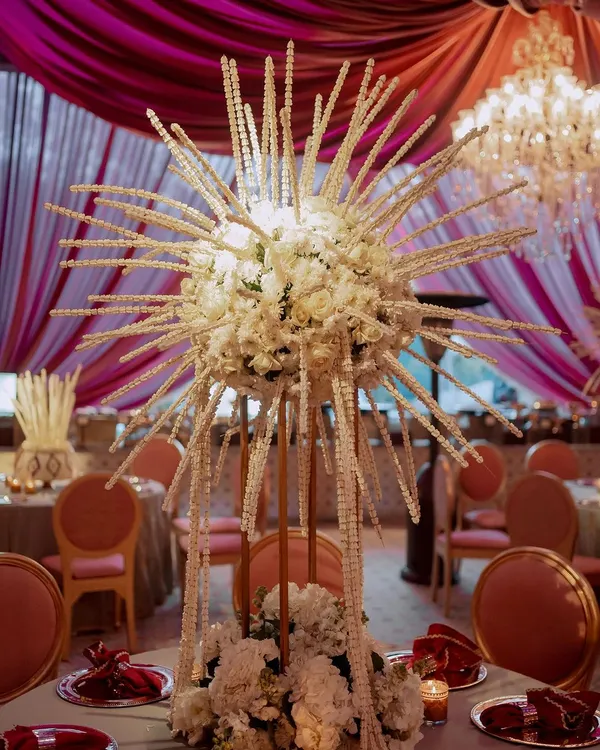 A unique and artistic centerpiece featuring a sphere of white flowers with radiating strings of pearls. This custom creation adds a dramatic and modern touch to the wedding tablescape.