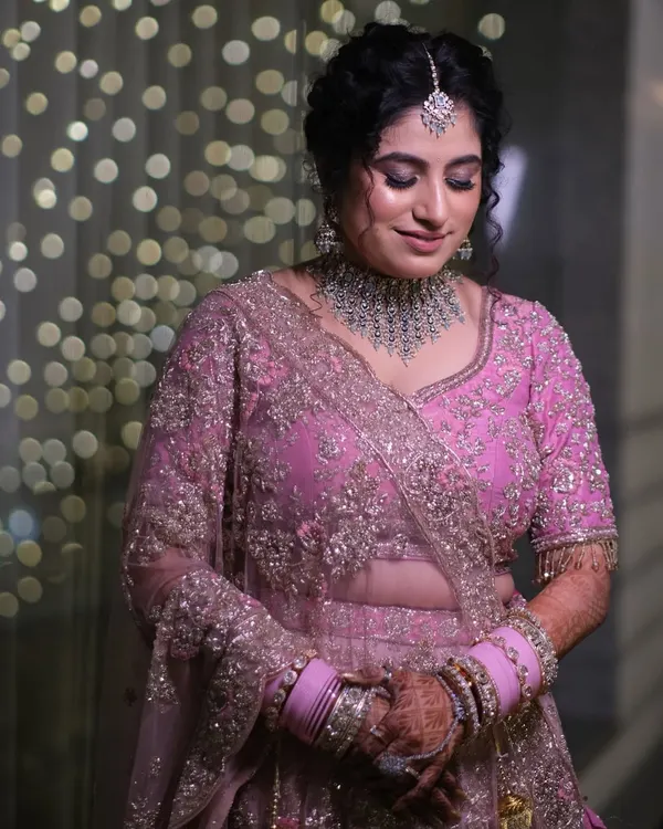 A beautiful bride in her pink lehenga, surrounded by the soft glow of bokeh lights. This portrait captures her serene happiness just before the main event.