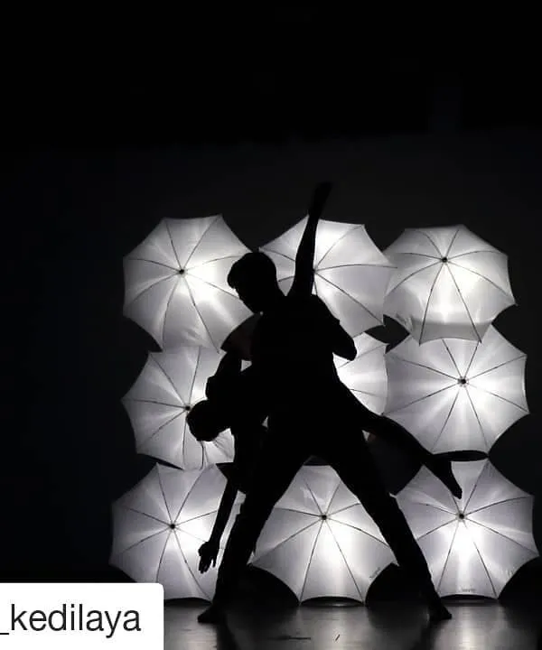 A silhouette of two dancers performing a contemporary piece against a backdrop of illuminated white umbrellas. This moment captures the artistry and creative staging from our annual "I Will Dance" showcase.