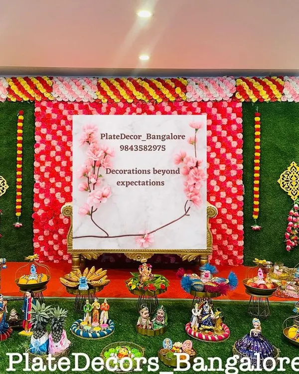 A full stage setup for a seer varisai ceremony, with a floral backdrop and a wide assortment of my decorated platters arranged neatly on a green turf.