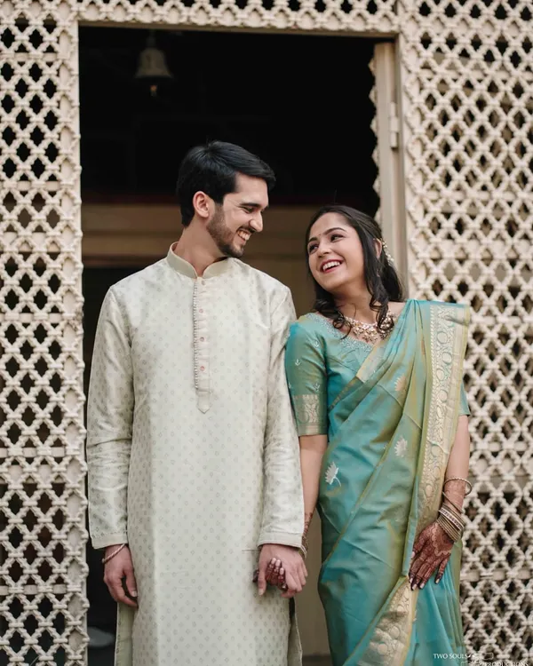 A shared glance filled with love, framed by the intricate details of a traditional haveli doorway. We love using architectural elements to tell a story.