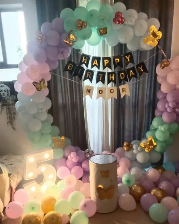 A dreamy butterfly-themed party for a 5th birthday. This cozy home setup includes a circular balloon arch in pastel pink, purple, and mint green, accented with gold butterflies and a light-up number '5'.