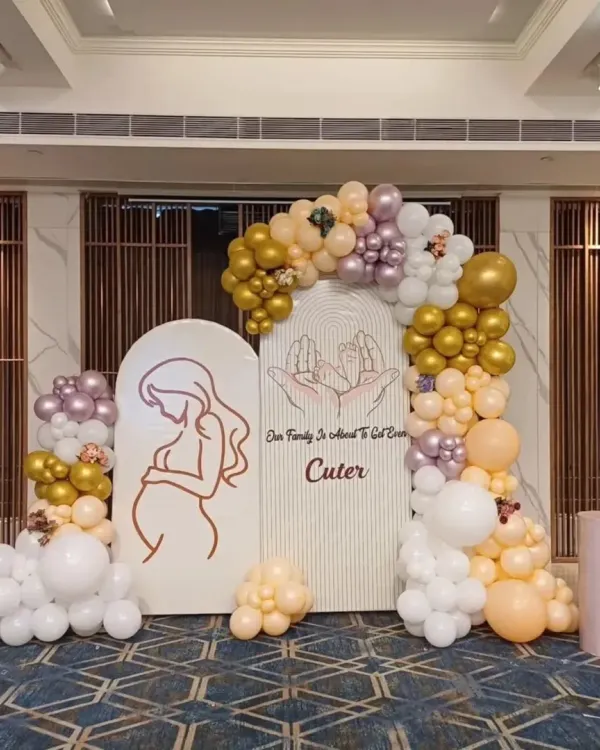 This elegant baby shower backdrop features two arched panels with custom messages and graphics. The organic balloon garland in white, gold, and mauve adds a touch of modern sophistication.