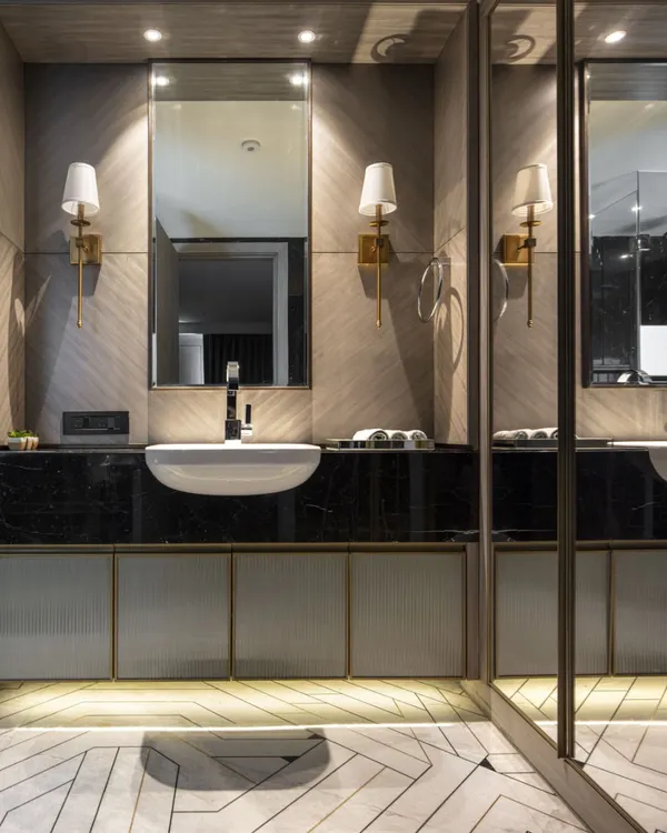 A bathroom in the Jor Bagh Residence featuring a geometric Indian stonework floor pattern. The design combines a dark marble countertop with fluted glass cabinetry and warm brass fixtures for a timelessly elegant look.