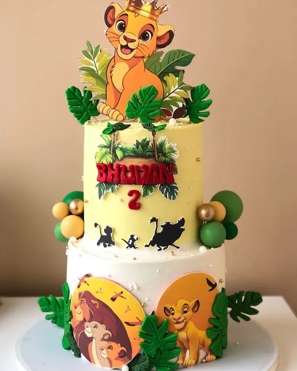A vibrant two-tiered Lion King cake for a second birthday, featuring Simba and silhouettes of other characters from the movie.