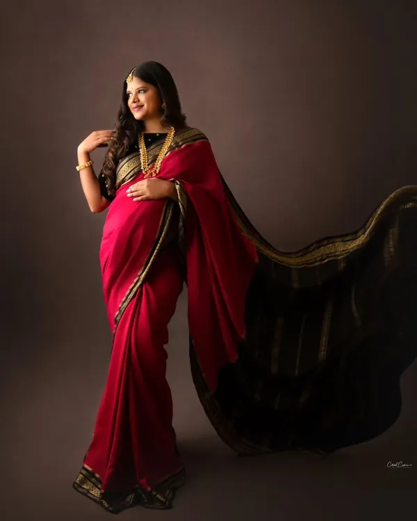 A stunning portrait of a mom-to-be in a traditional red and black saree. The flowing pallu adds a beautiful, dynamic element to the shot.