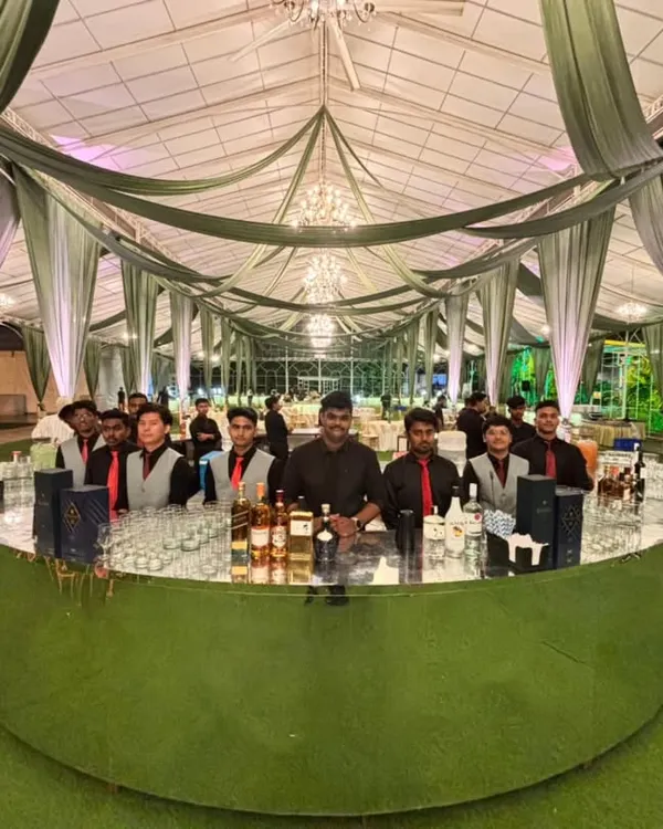 This is our personal bar on wheels, ready to serve at any large-scale wedding or event. Here you can see our stunning circular green shimmer bar, fully stocked and staffed by our professional team, creating an impressive centerpiece for a grand celebration.