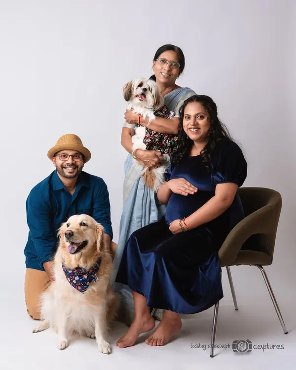 A full family portrait celebrating three generations and the furry family members. The expecting couple is joined by a grandparent and their two dogs for a memorable studio maternity photo.