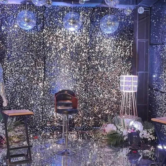 A view of the sangeet party setup, featuring a high-top bar stool and floral arrangements against the silver sequin backdrop.