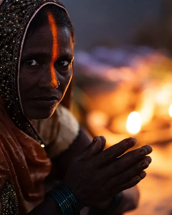 A woman's intense gaze during the Chhath Mahaparv festival in Delhi, her face marked with the sacred sindoor. The low light of the diyas highlights the deep personal connection of the ritual.