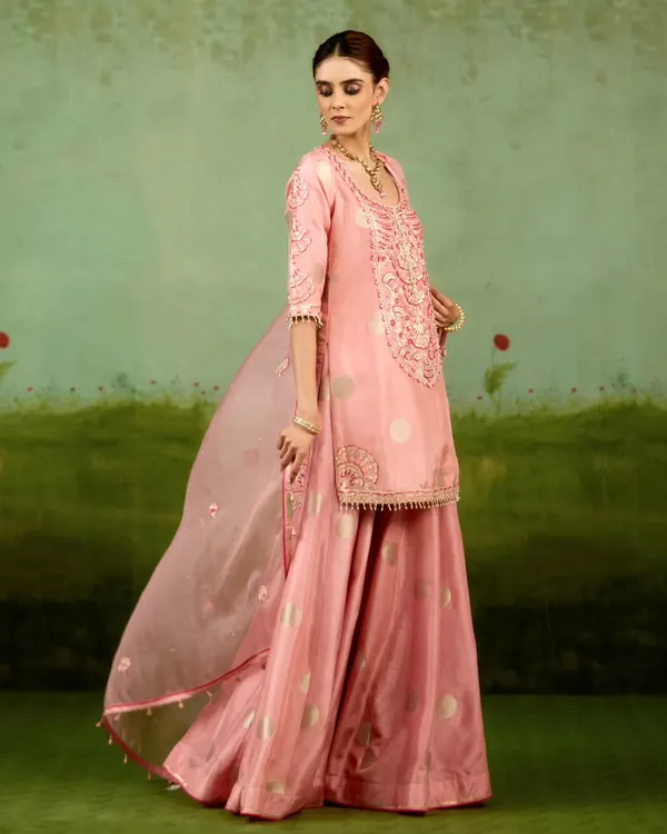 This playful yet refined sharara set in soft pink showcases fluid lines and hand-finished detail. The sheer dupatta adds a touch of grace, making it perfect for a daytime festive event.