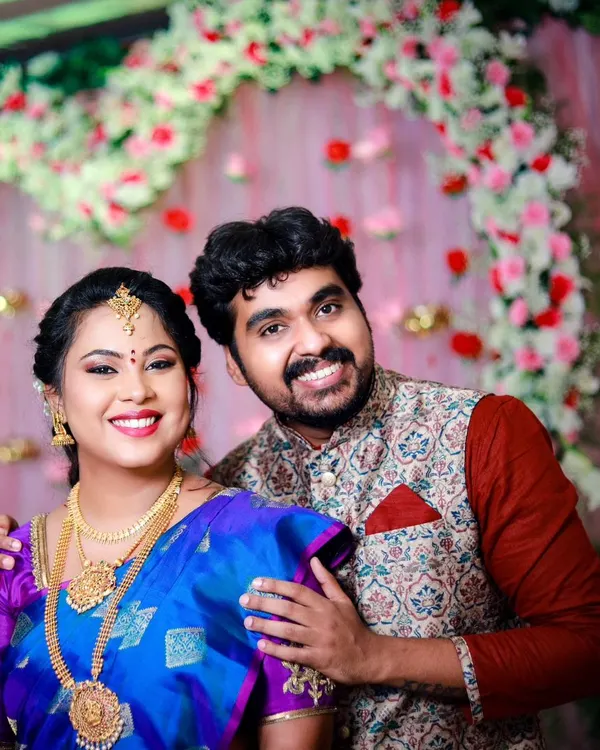 A happy couple portrait from an engagement ceremony. The vibrant floral backdrop and their joyful smiles perfectly capture the celebratory mood.