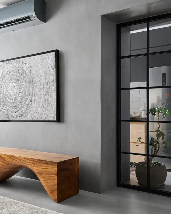 The living room of Zen House features grey micro-concrete floors and walls, which create a seamless, monolithic backdrop. This is balanced by the warmth of a statement wooden bench made from a single piece of East Indian walnut.