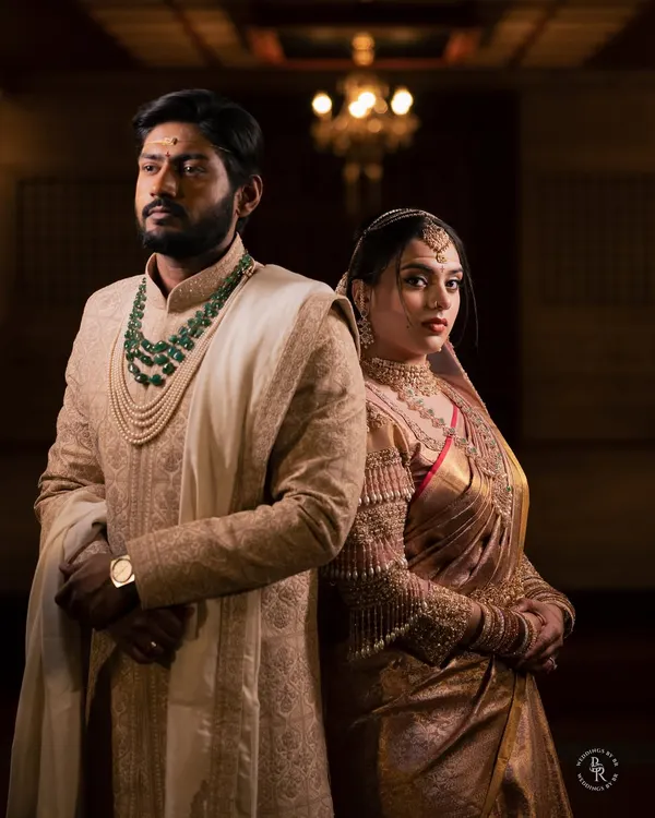 A powerful and regal portrait of a couple on their wedding day. The dramatic, low-key lighting emphasizes their stunning traditional attire and their strong, united presence.