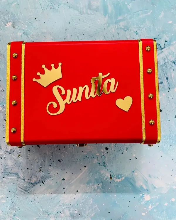 This vibrant red keepsake trunk is personalized with a name, a crown, and a heart charm. The gold accents and hardware give it a luxurious, vintage feel.