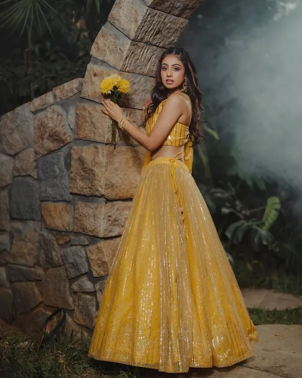 This image captures a dreamy, romantic mood. The soft lighting and natural setting complement the shimmering yellow lehenga, making it ideal for a pre-wedding or festive collection.