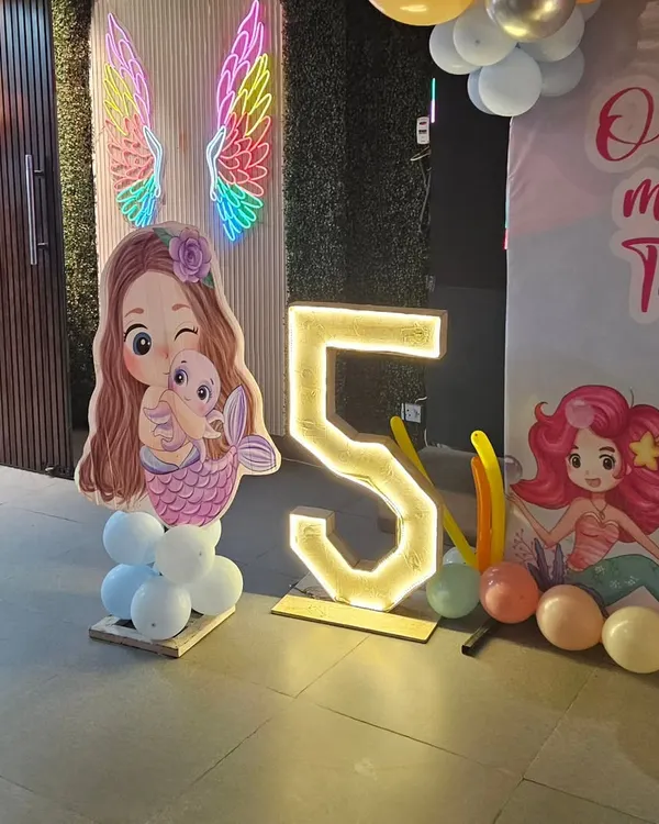 A magical mermaid theme for a 5th birthday, complete with a mermaid cutout, a light-up number "5", and colorful neon angel wings.