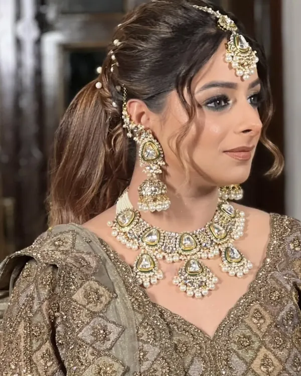 A beautiful bride styled in a heavy Polki kundan necklace set with matching jhumkas and maang tikka. The neutral tones of this jewellery make it a versatile choice for any bridal lehenga.