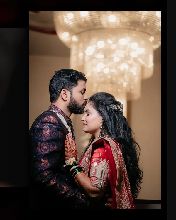 A classic reception portrait under a grand chandelier. The groom's tender kiss on the bride's forehead is a moment of pure romance.
