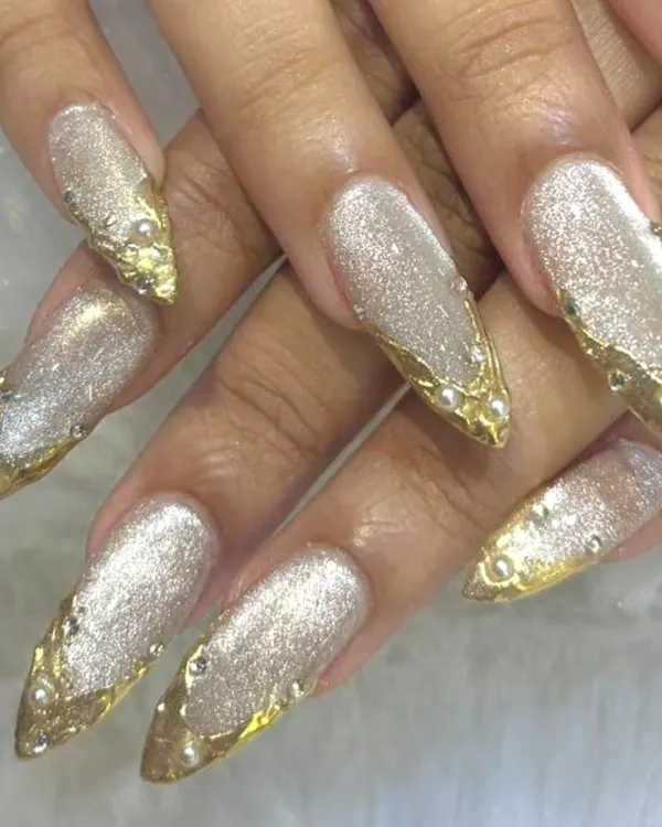 We crafted these dramatic stiletto nail extensions for a truly showstopping look. This design features a shimmering glitter base, meticulously applied 3D gold accents, and delicate pearl embellishments, making it a perfect choice for a bride or any grand celebration.