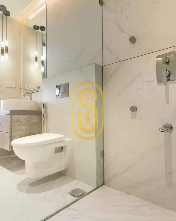 A bright and minimalist bathroom design using white marble-patterned tiles. The space features a wall-mounted toilet and a floating vanity to maximize floor space, with a glass partition for the shower area.