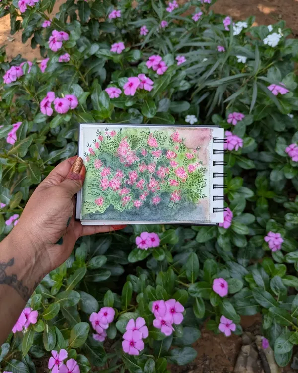 Here's a fun shot from my travels, holding my watercolor painting of periwinkles right in front of the bush that inspired it. I love capturing the beauty of nature as I see it, creating a lasting memory on paper.