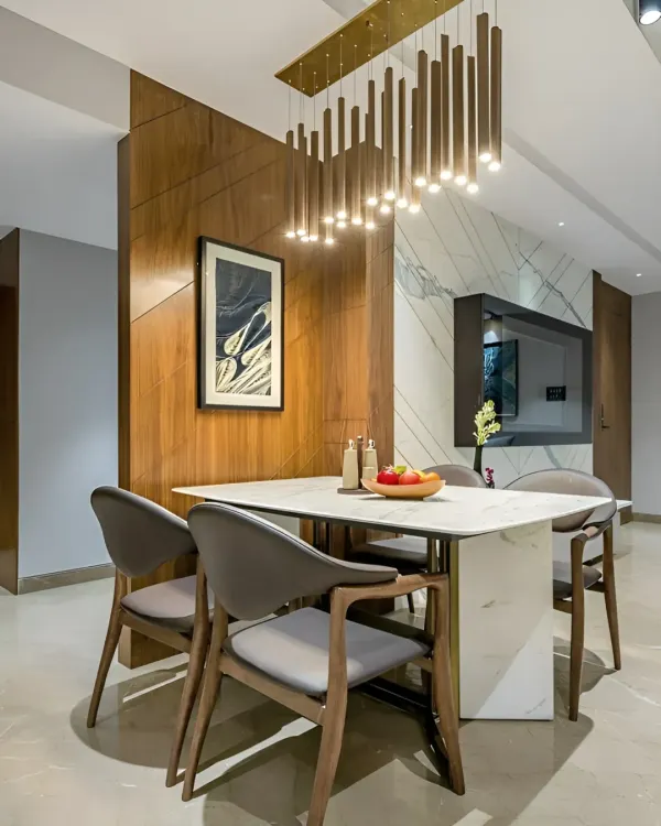 A modern dining setup defined by a wooden partition wall that separates it from the living area. The statement pendant light fixture and marble-top table create an elegant space for family meals.