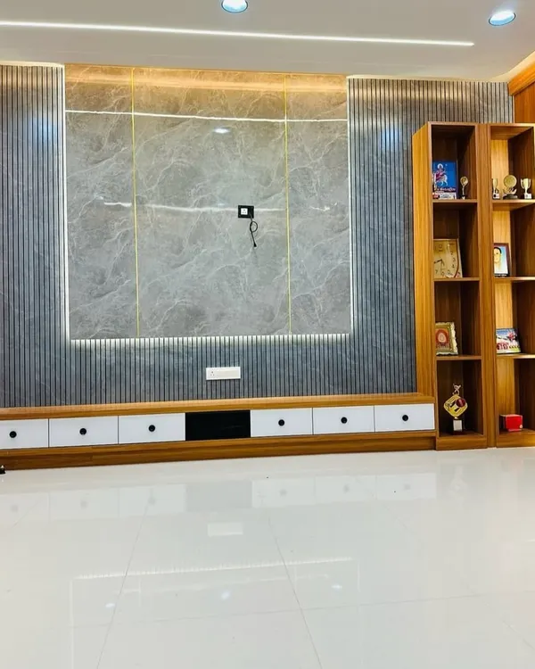 A large, wall-mounted TV unit featuring a grey marble-finish center panel flanked by dark grey fluted panels. The unit includes a long, low-profile console with white drawers and an attached wooden bookshelf for display.