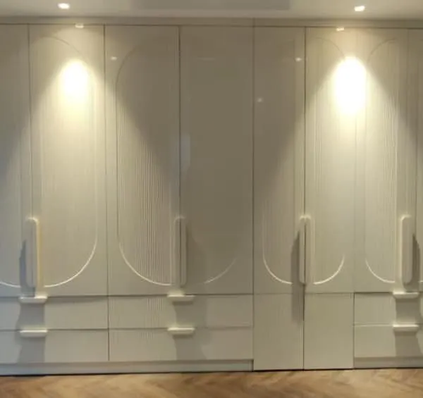 We designed this expansive floor-to-ceiling wardrobe to be a statement piece. It features a flawless high-gloss PU finish with custom CNC-milled circular patterns and integrated handles, creating a seamless and luxurious facade.