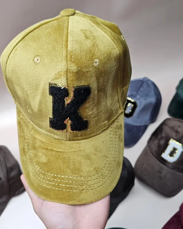 A close-up of our custom suede cap, showing the textured fabric and the detailed sequin initial patch.