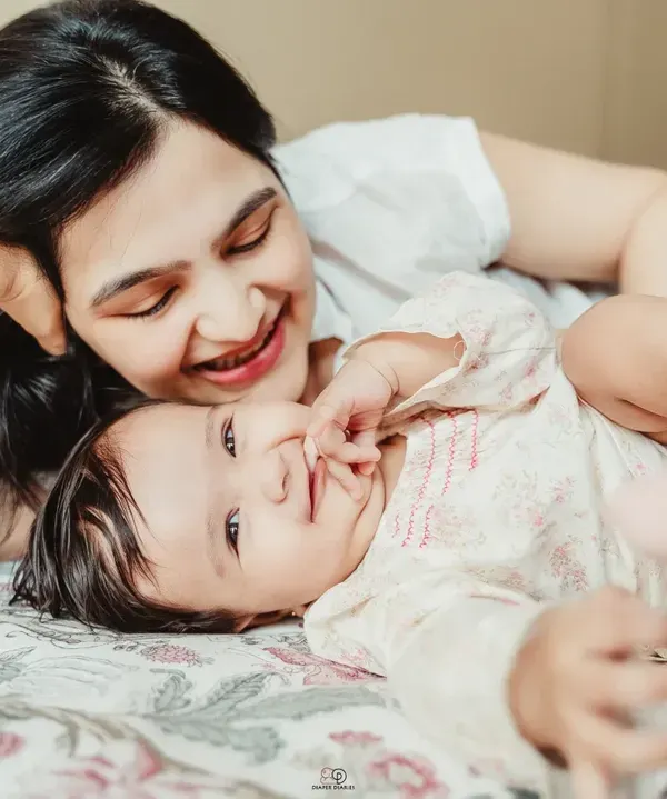 A series of candid shots from an in-home lifestyle session. A mother and her baby are playing and laughing on a bed, showcasing the natural, joyful moments I aim to capture.