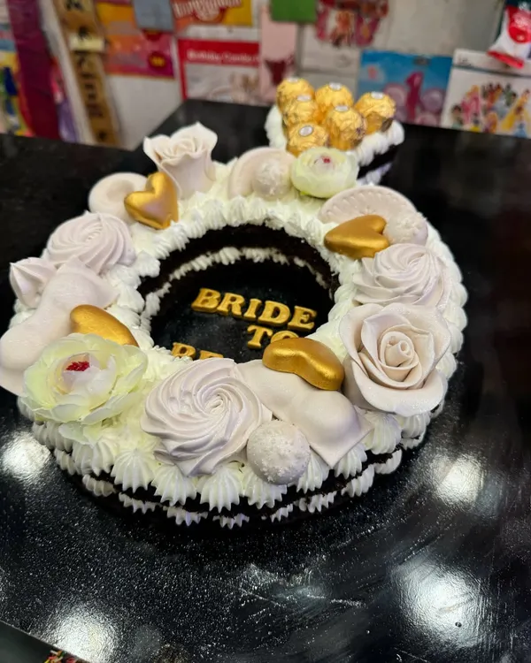 A stunning ring-shaped cake for a 'Bride to Be' party. This custom design features delicate frosting, golden hearts, and is topped with Ferrero Rocher chocolates for an extra touch of luxury.