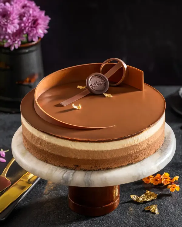 A multi-layered chocolate mousse cake with a glossy finish and an elegant chocolate swirl, presented on a marble cake stand for a sophisticated dessert shot.