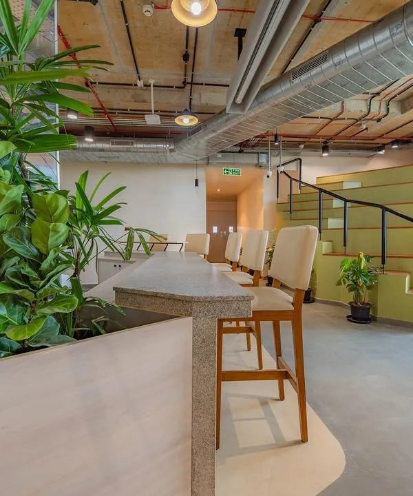 This multi-functional breakout space features tiered amphitheater-style seating for presentations and a high-top counter overlooking the area. Abundant plants and natural materials create a refreshing, campus-like feel.