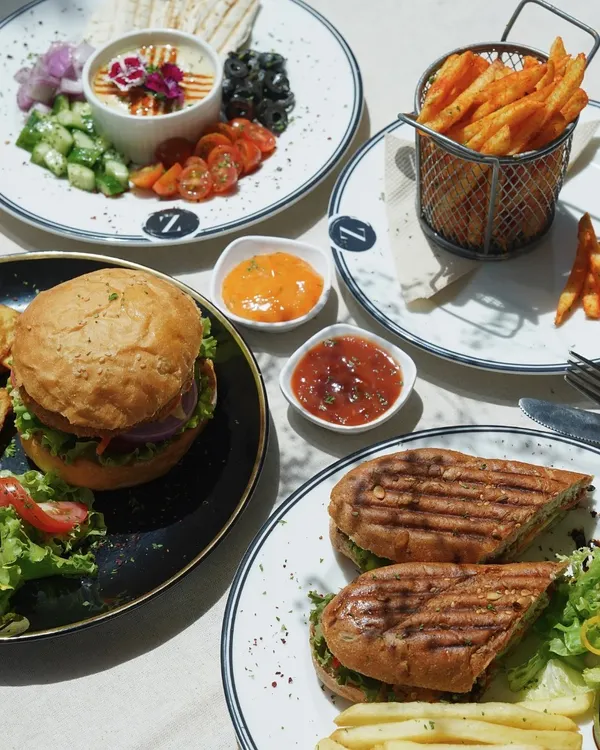 My lunch spread is designed for sharing and savoring. It features a juicy burger with potato wedges, a grilled panini, a fresh hummus platter, and a basket of crispy fries.