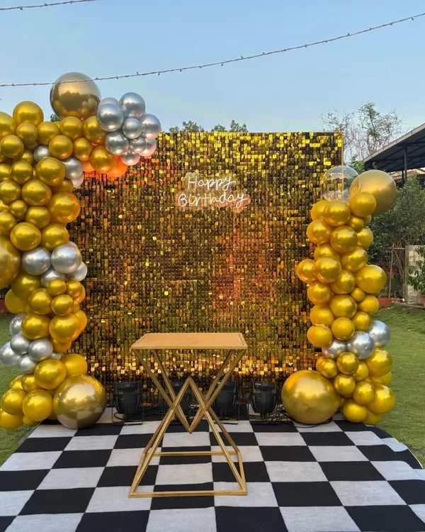 We create stunning photo backdrops for any occasion, like this glamorous gold shimmer wall with balloon pillars, perfect for an outdoor 40th birthday celebration.