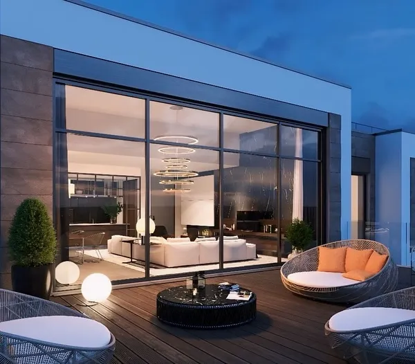 An exterior view of a modern terrace lounge, showing the structure's clean lines and integration with the building. The open deck features comfortable seating, perfect for enjoying the evening air.