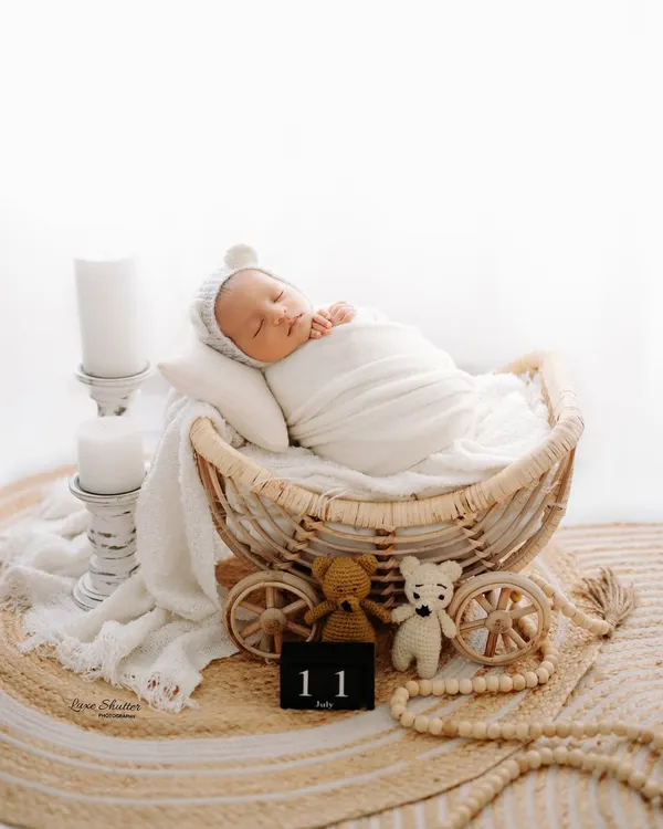 A peaceful 11-day-old newborn sleeping in a rustic wicker pram. We use a variety of props and soft, neutral tones to create these timeless newborn portraits.