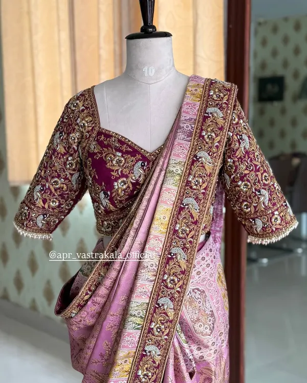 A breathtaking bridal blouse in magenta, completely covered in intricate zardosi and threadwork. The design features peacock and floral motifs, perfect for a grand wedding ceremony.