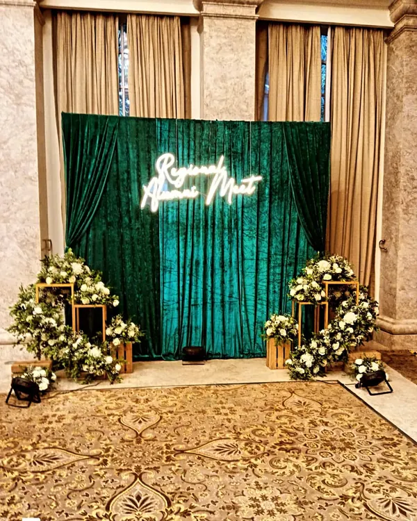 This is the 'Regional Alumni Meet' setup in natural light. The rich green velvet backdrop and classic white floral arrangements look just as impressive without special lighting, showing the quality of the materials.