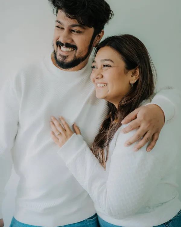 A simple, happy moment from a casual at-home shoot. The coordinated white sweaters and jeans create a clean, timeless look, while their genuine smiles radiate warmth and affection.